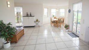Una cocina amplia con gabinetes blancos, un comedor con una mesa redonda y sillas, y una planta en maceta.