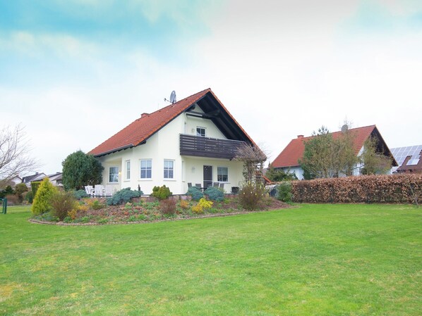 A two-story house with a red roof, a balcony, and a well-maintained garden. - Ferienhaus in Hessen mit großem Garten (Vöhl-Buchenberg)