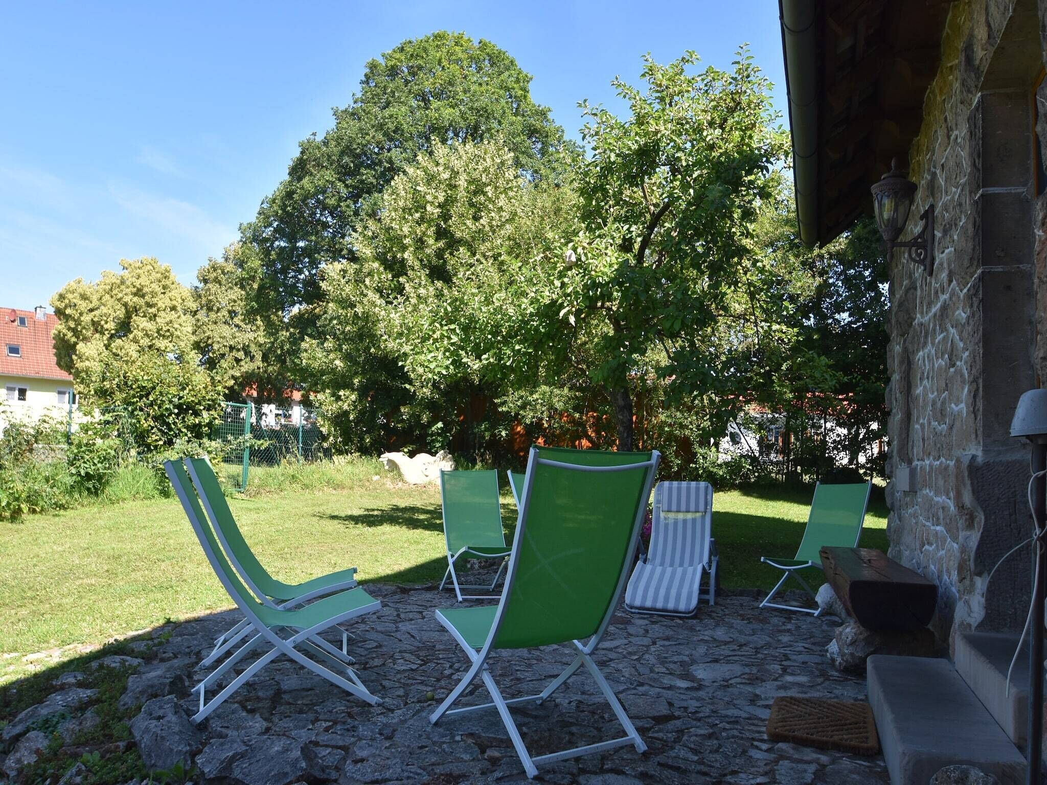 A patio area with stone flooring, green lounge chairs, and a stone wall.