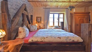 Une chambre à coucher rustique avec un lit en bois, des murs en pierre et une grande fenêtre.