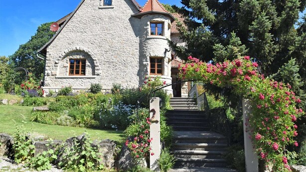Une maison en pierre avec un toit en pente, une petite fenêtre et un escalier menant à l’entrée.