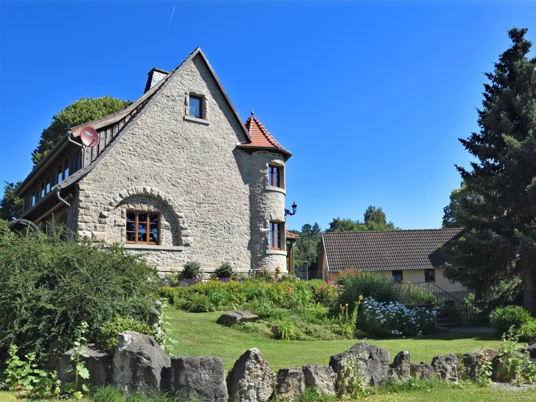 Uma casa de pedra com um telhado inclinado, uma torre e um jardim com pedras e plantas.
