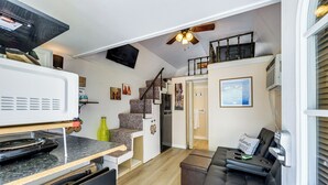 Ett kompakt bostadsutrymme med ett litet kök, en soffa, en trappa och en takfläkt.