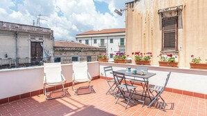 A terrace with a table and chairs, potted plants, and a building with a tiled roof in the background. - Casa Brunaccini con terrazza by Wonderful Italy (Palermo)