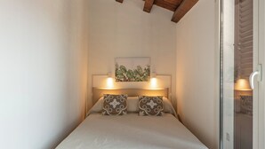 A bedroom with a wooden ceiling, a bed with a quilted mattress, two pillows, a bedside table with a lamp, and a sliding glass door. - Casa Brunaccini con terrazza by Wonderful Italy (Palermo)