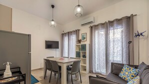 A modern living room with a sofa, a dining table with chairs, a TV mounted on the wall, and a window with curtains. - Casa Brunaccini con terrazza by Wonderful Italy (Palermo)