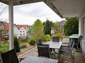 Un espace extérieur aménagé, abrité et doté de tables et de chaises, offrant une vue sur un village avec ses maisons traditionnelles et sa verdure.