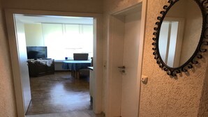 Un corridoio che conduce a una sala da pranzo con tavolo e sedie, una televisione e una porta con uno specchio decorativo.