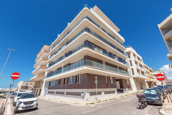 Un edificio de varios pisos con balcones, coches aparcados y un cielo azul despejado.