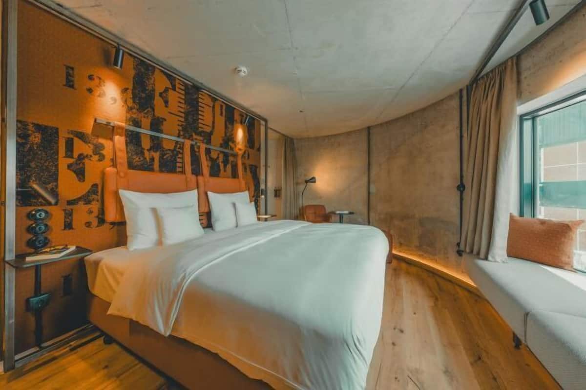 Un dormitorio con una cama grande, una mesita de noche, una ventana con cortinas y una pared con diseño decorativo.