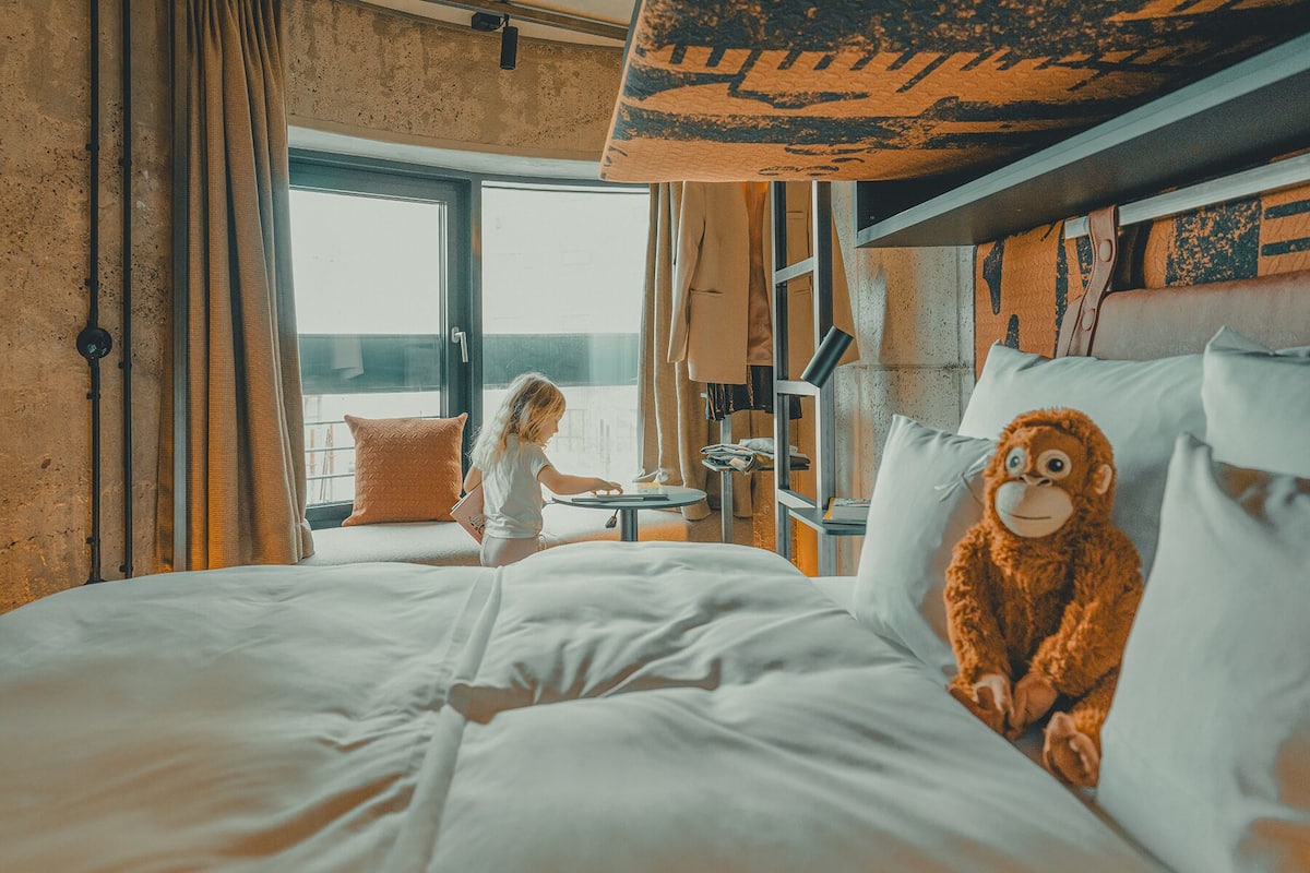 Un dormitorio con una cama grande, una ventana con cortinas y vistas al exterior, además de un peluche de mono sobre las almohadas.