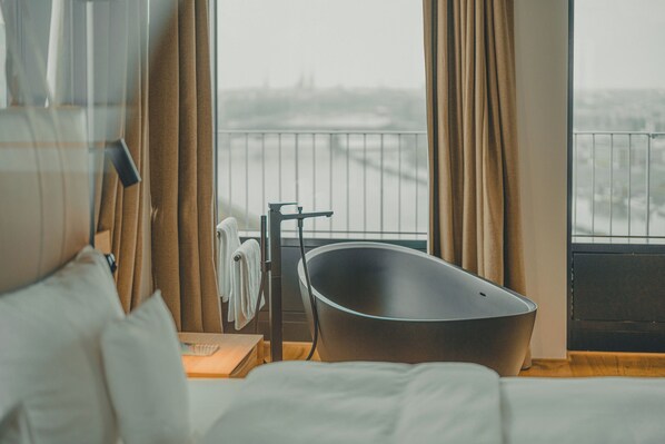 Une chambre d’hôtel moderne dotée d’une grande fenêtre, d’une baignoire et offrant une vue sur le paysage urbain.