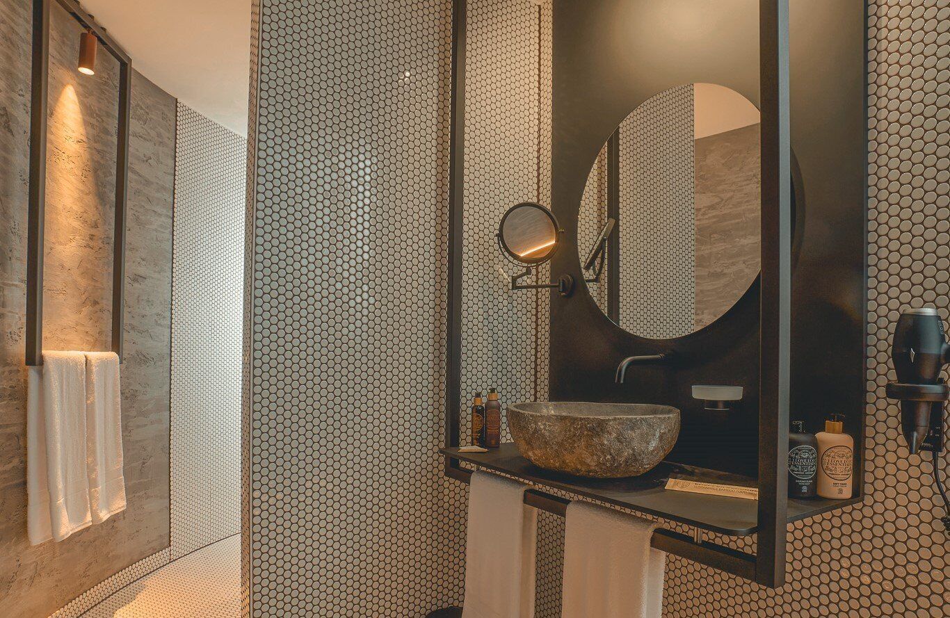 Un baño con un espejo grande, un lavamanos redondo y un perchero para toallas.
