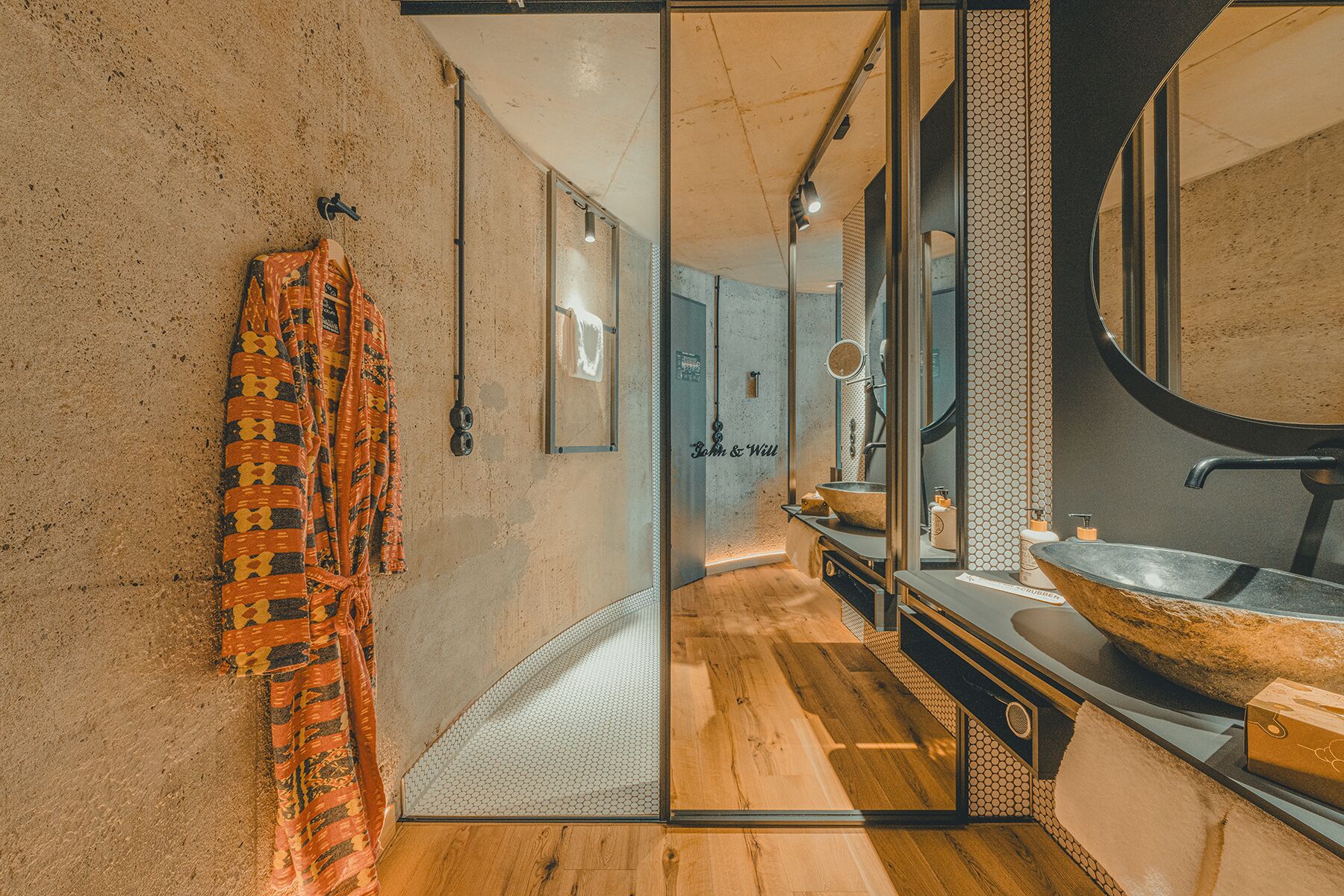A modern bathroom with a wooden floor, a large mirror, and a unique patterned towel hanging on the wall.