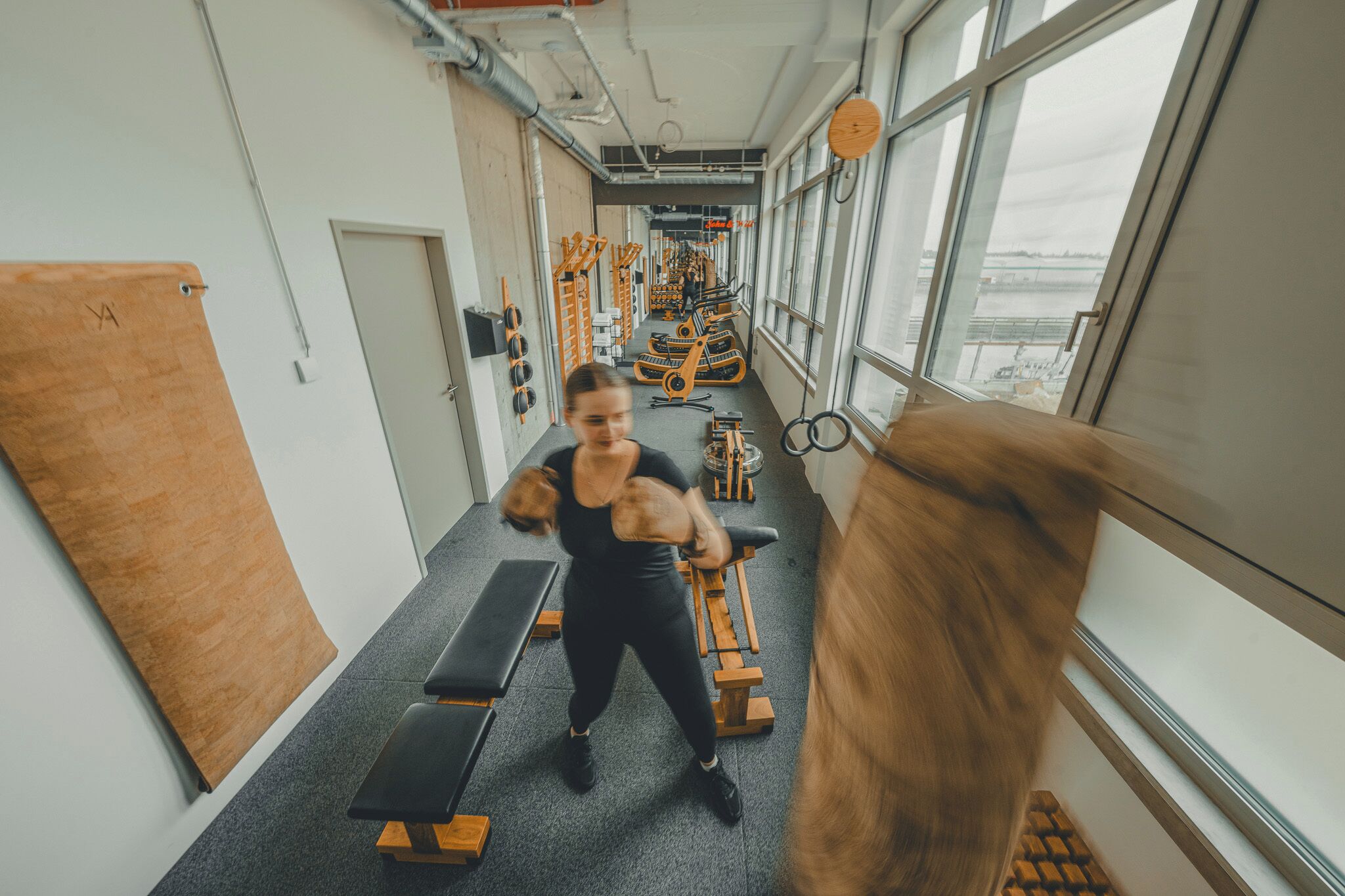 Une salle de sport équipée de machines, de bancs et offrant une vue sur une rivière grâce à de grandes fenêtres.
