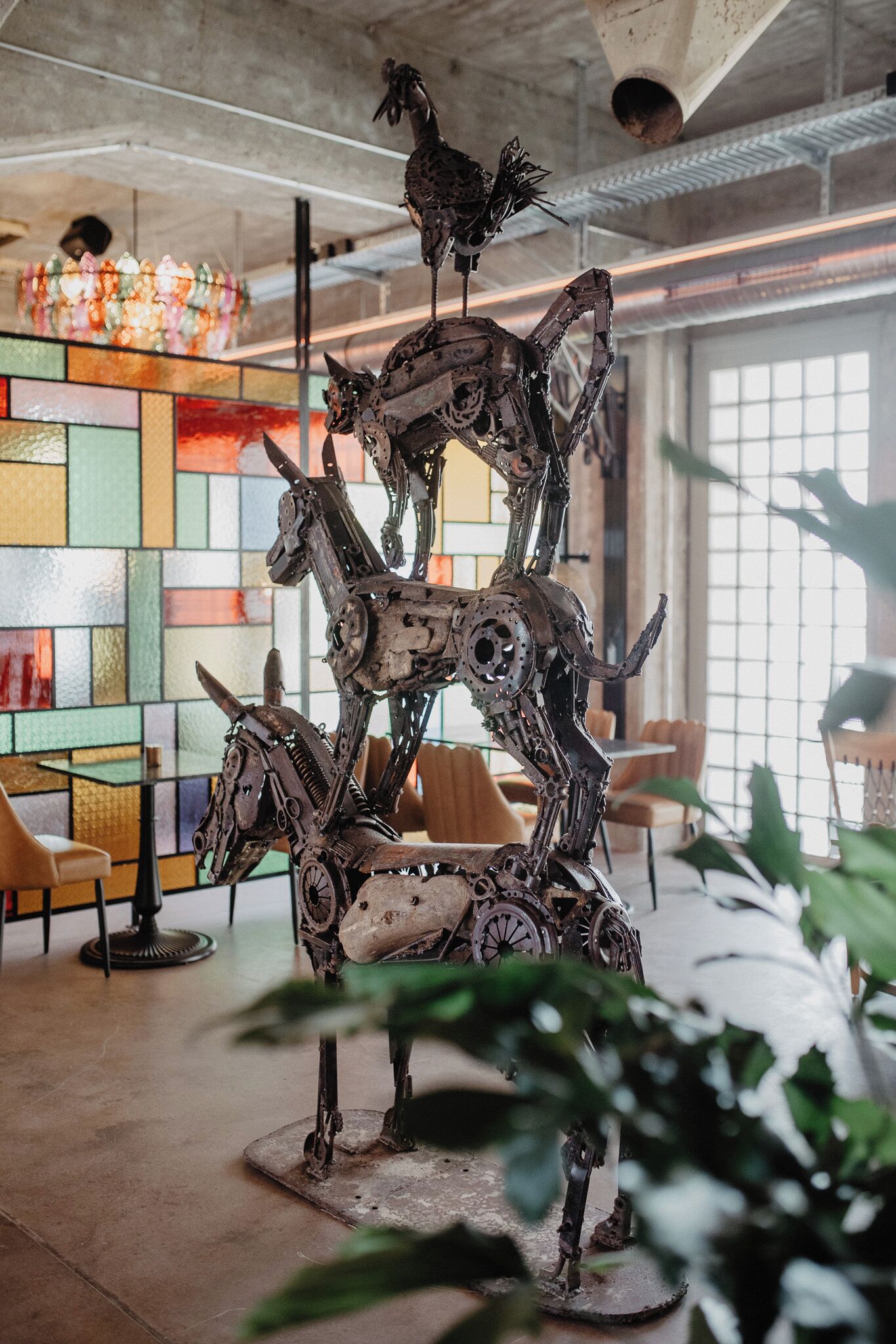 A sculpture of mechanical horses in a modern interior space with a colorful stained glass wall and a large window.