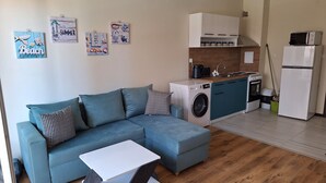 Un appartement moderne avec un canapé gris, une petite table blanche, un lave-linge, une cuisinière et un réfrigérateur.