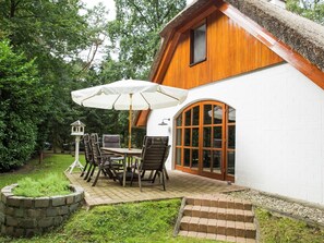 Una casa de madera con fachada blanca, un amplio ventanal arqueado y un patio con mesa y sillas.