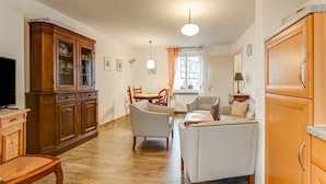 A spacious living room with a wooden cabinet, a television, a dining table with chairs, and a sofa. - Apartment with wellness oasis (Hellenthal- Reifferscheid)