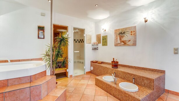 A modern bathroom with a large bathtub, two sinks, and a tiled floor. - Apartment with wellness oasis (Hellenthal- Reifferscheid)