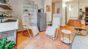 A modern kitchen with white appliances, a refrigerator, and a sink. There are two white chairs and a small table. The room has tiled flooring and a staircase leading to another area. - Apartment with wellness oasis (Hellenthal- Reifferscheid)