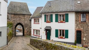 A cobblestone street with traditional European architecture, including a stone archway and buildings with white walls and green shutters. - Apartment with wellness oasis (Hellenthal- Reifferscheid)