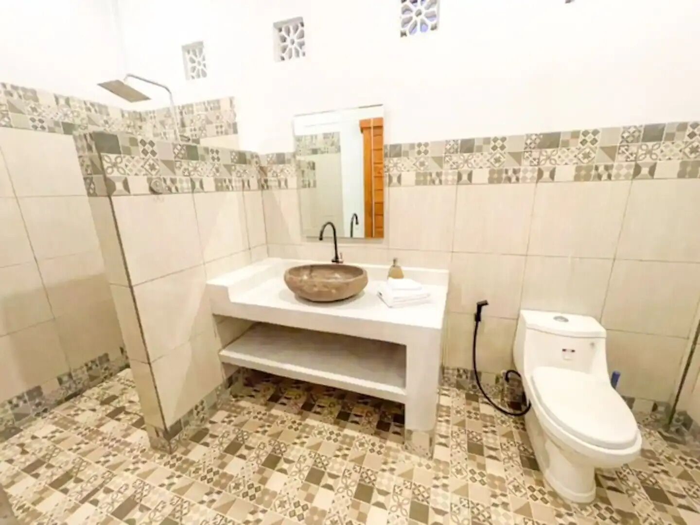 A bathroom with a white sink, a large mirror, and a toilet. The floor has patterned tiles.