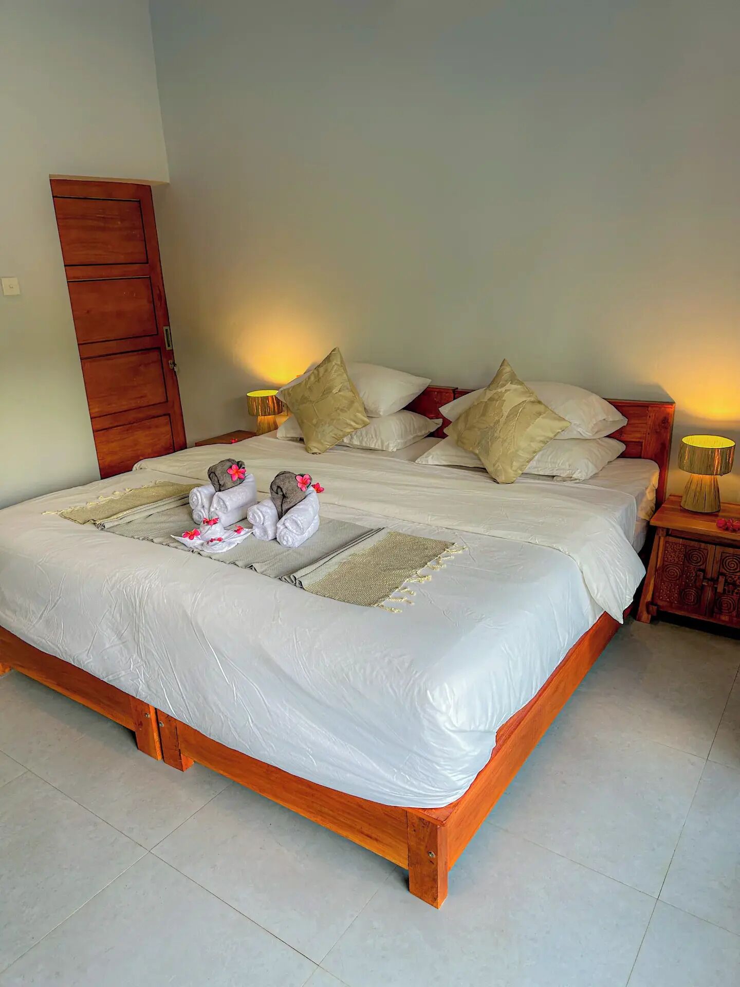 A neatly made bed with white linens, a wooden headboard, and two bedside lamps.