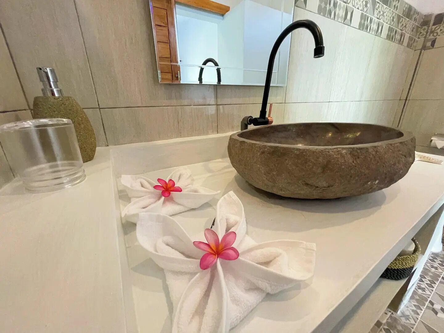 A bathroom with a stone basin sink, a mirror, and two towels with flowers.