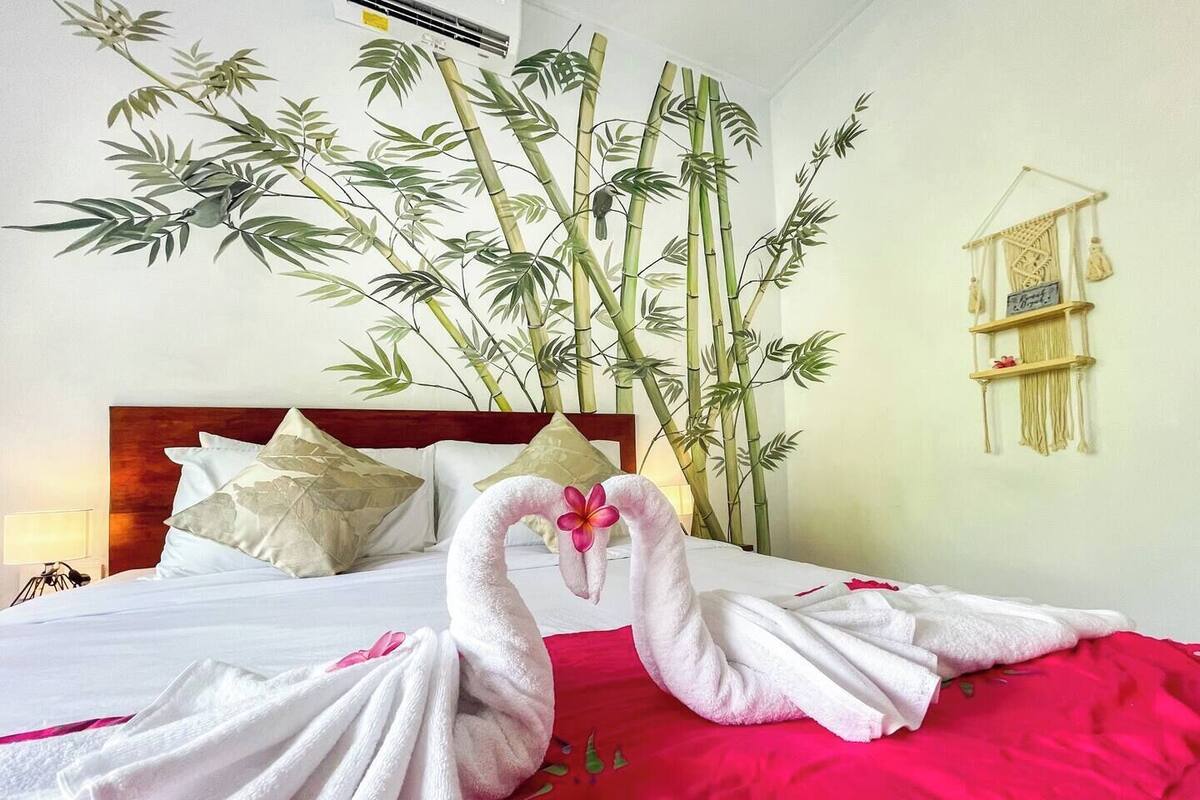 A hotel room with a bed, a large bamboo plant, and a macrame wall hanging.