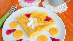 A plate of crepes with fruit and a pink drink on a wooden table. - Rumah Diyah (Karangasem)