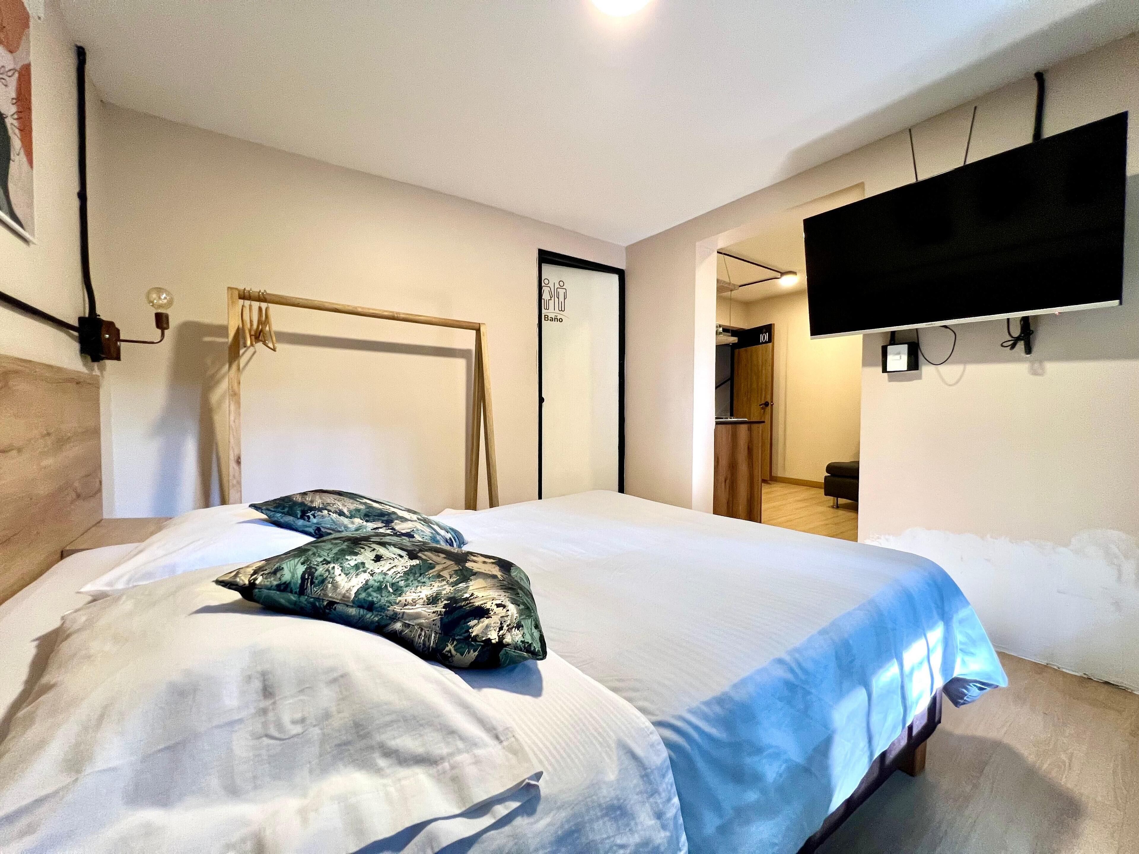Ein Hotelzimmer mit einem Bett, einem an der Wand montierten Fernseher, einer Holztür und einer Leuchte.