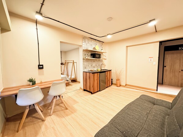 A modern living room with a sofa, dining area with chairs, a kitchen with a microwave, and a door labeled "105". - Niddo by Roots Rentals (Medellín)