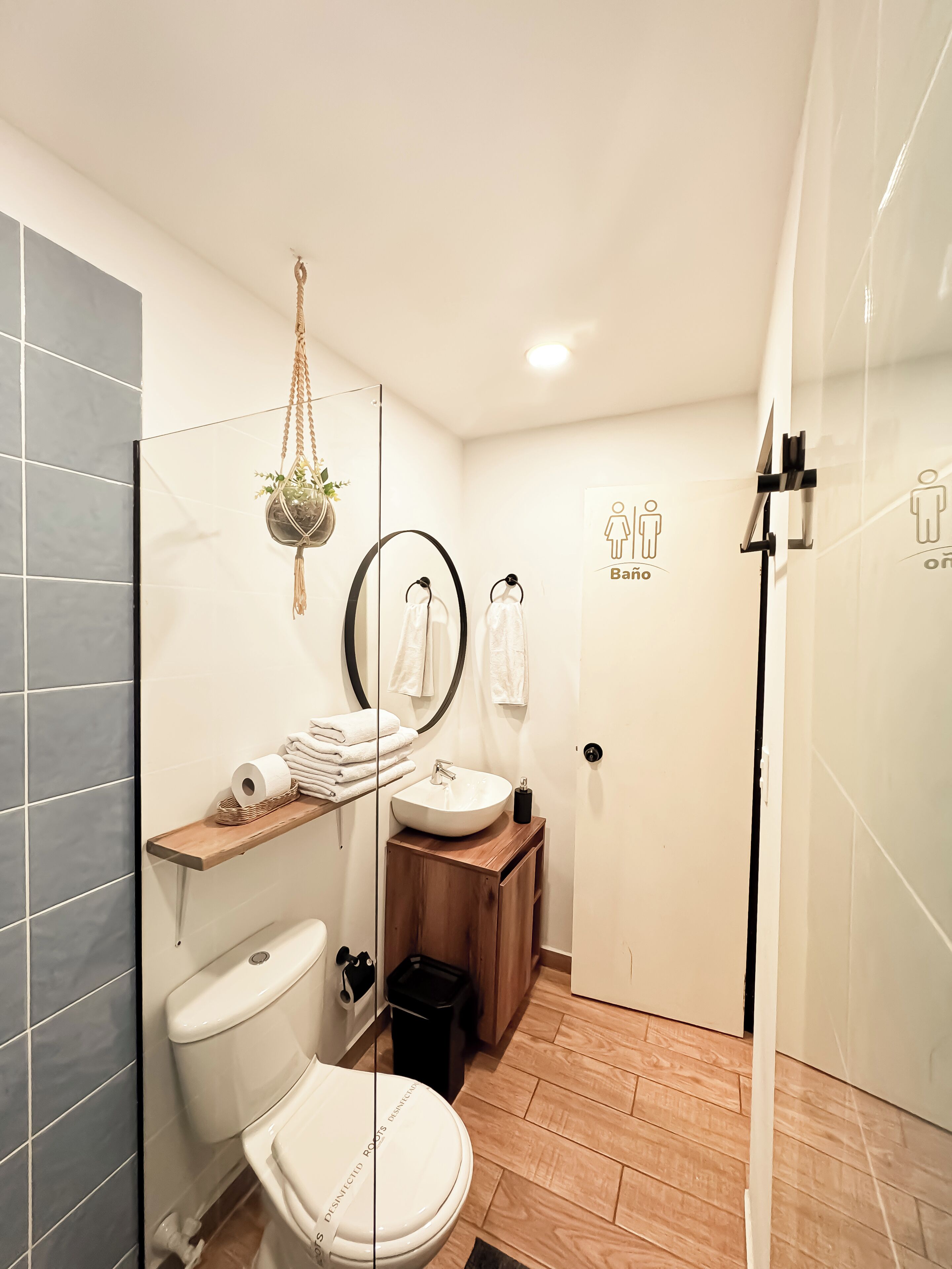 A modern bathroom with a toilet, sink, and shower. There are towels and a hanging plant.
