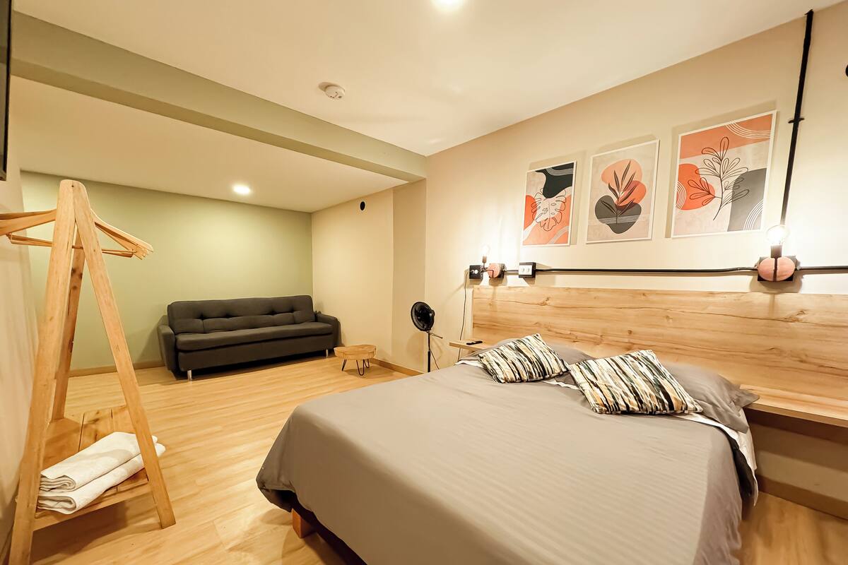 Une chambre à coucher moderne avec un lit, une balançoire en bois, un canapé et des œuvres d’art accrochées au mur.