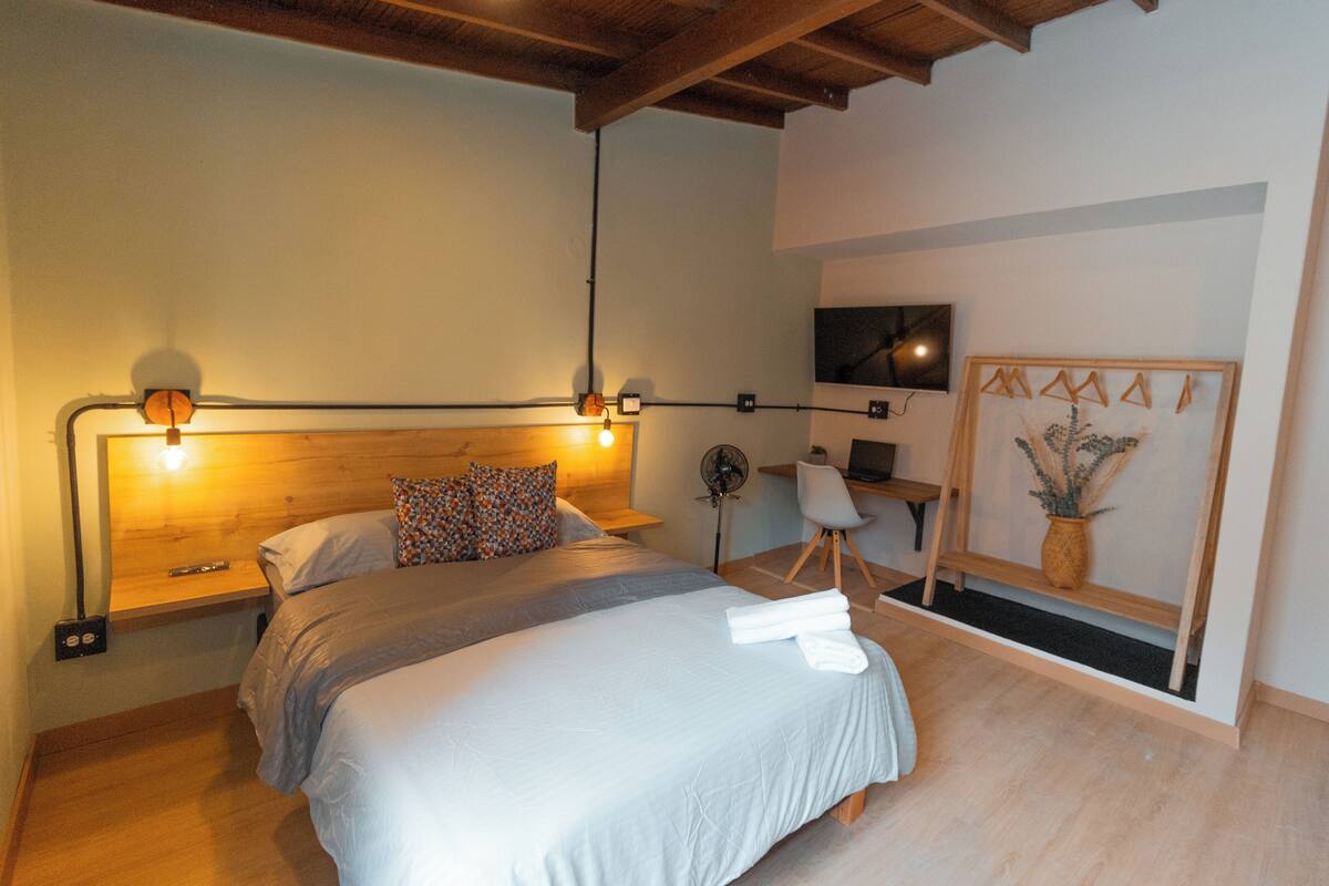 Une chambre à coucher comprenant un lit, des tables de chevet, un bureau, une chaise, un téléviseur et une œuvre d’art accrochée au mur.