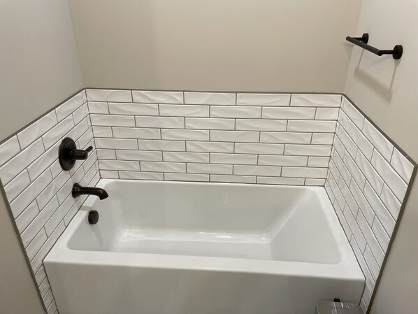 A white bathtub with black fixtures, surrounded by white subway tile walls. - Modern, Quiet, & Comfortable Stay - Near E-Town Sports Park, BluOval SK & Eats! (Glendale)