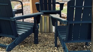 Un espace extérieur aménagé avec des chaises Adirondack et une table en métal, entouré de gravier et d’une terrasse en bois.