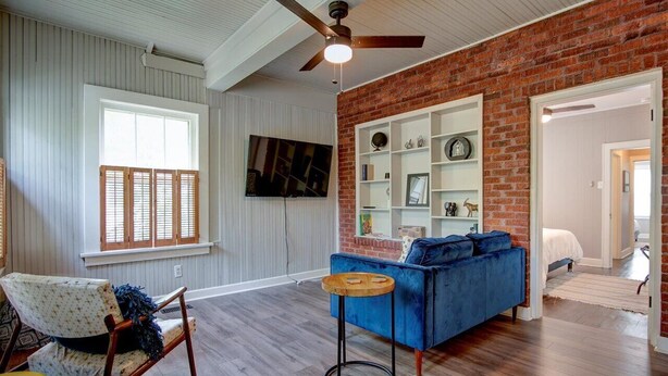 Un salon spacieux avec un canapé bleu, un plancher en bois, un mur en briques et un ventilateur de plafond.