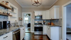 Une cuisine avec des armoires blanches, un four en acier inoxydable, un four à micro-ondes et une machine à café.
