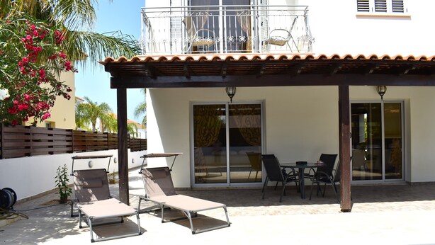 A poolside area with lounge chairs, a table, and a covered patio. - The Brilliant Villa Pernera (Pernera)