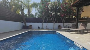 A rectangular swimming pool with clear blue water, surrounded by a tiled deck. There are lounge chairs and a pergola with a roof. - The Brilliant Villa Pernera (Pernera)
