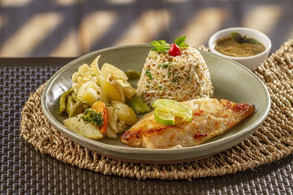 A plate of food with rice, vegetables, and a piece of chicken, served on a woven placemat. - Un Paso Del Mar (Ipojuca)