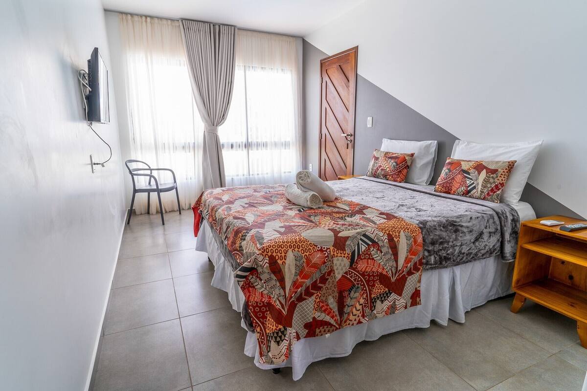 A bedroom with a bed, a chair, a wooden nightstand, and a door.