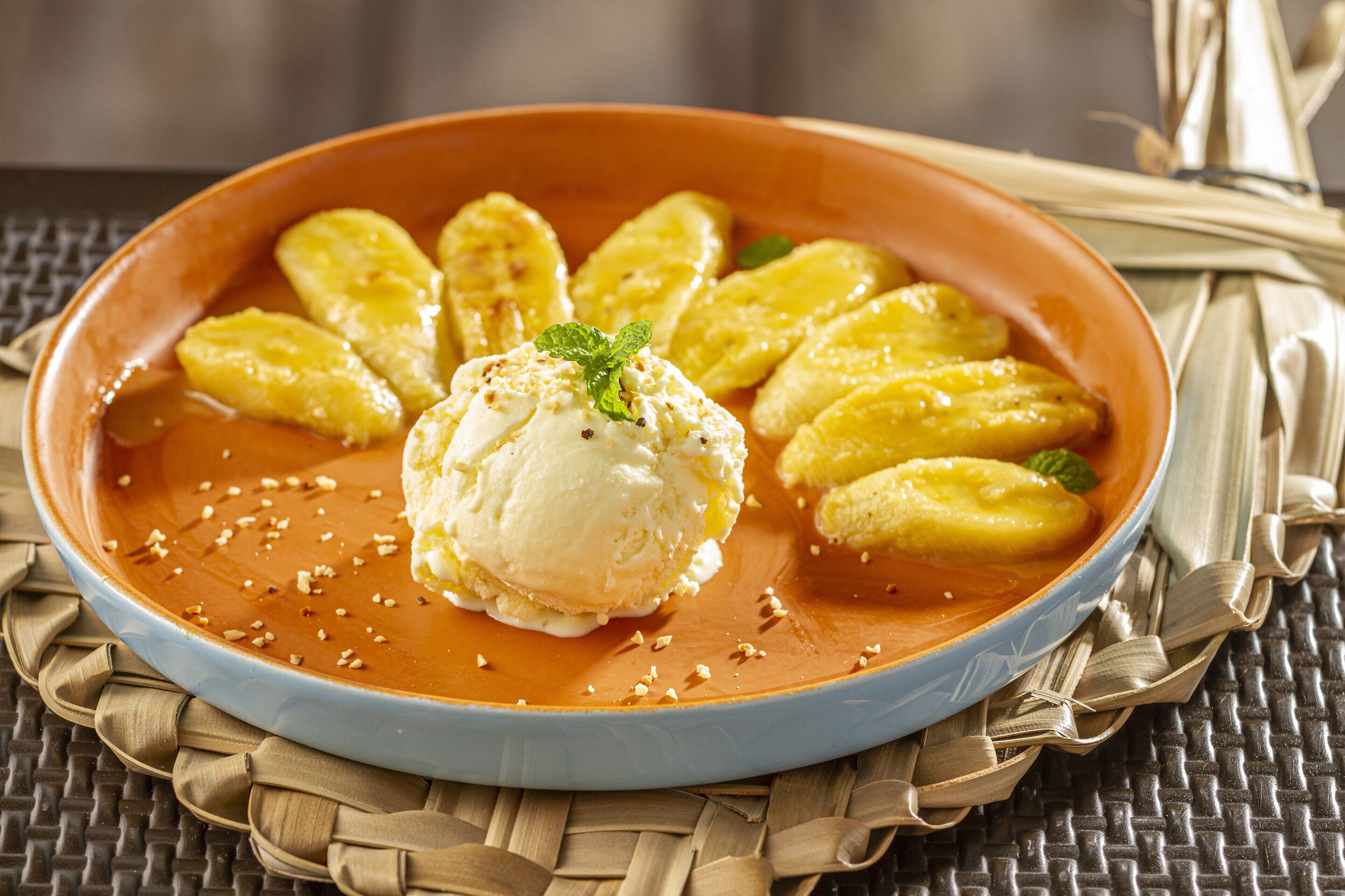 Un plato de postre con helado y rodajas de plátano sobre un tapete tejido.