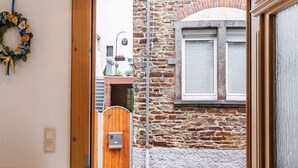 A view through a wooden door into a courtyard with a stone wall, a wooden gate, and a window with shutters. - Ferienwohnung in Ediger (Mosel) (Ediger-Eller)