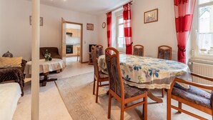 A cozy dining area with a round table, wooden chairs, and red curtains. A kitchen is visible in the background. - Ferienwohnung in Ediger (Mosel) (Ediger-Eller)