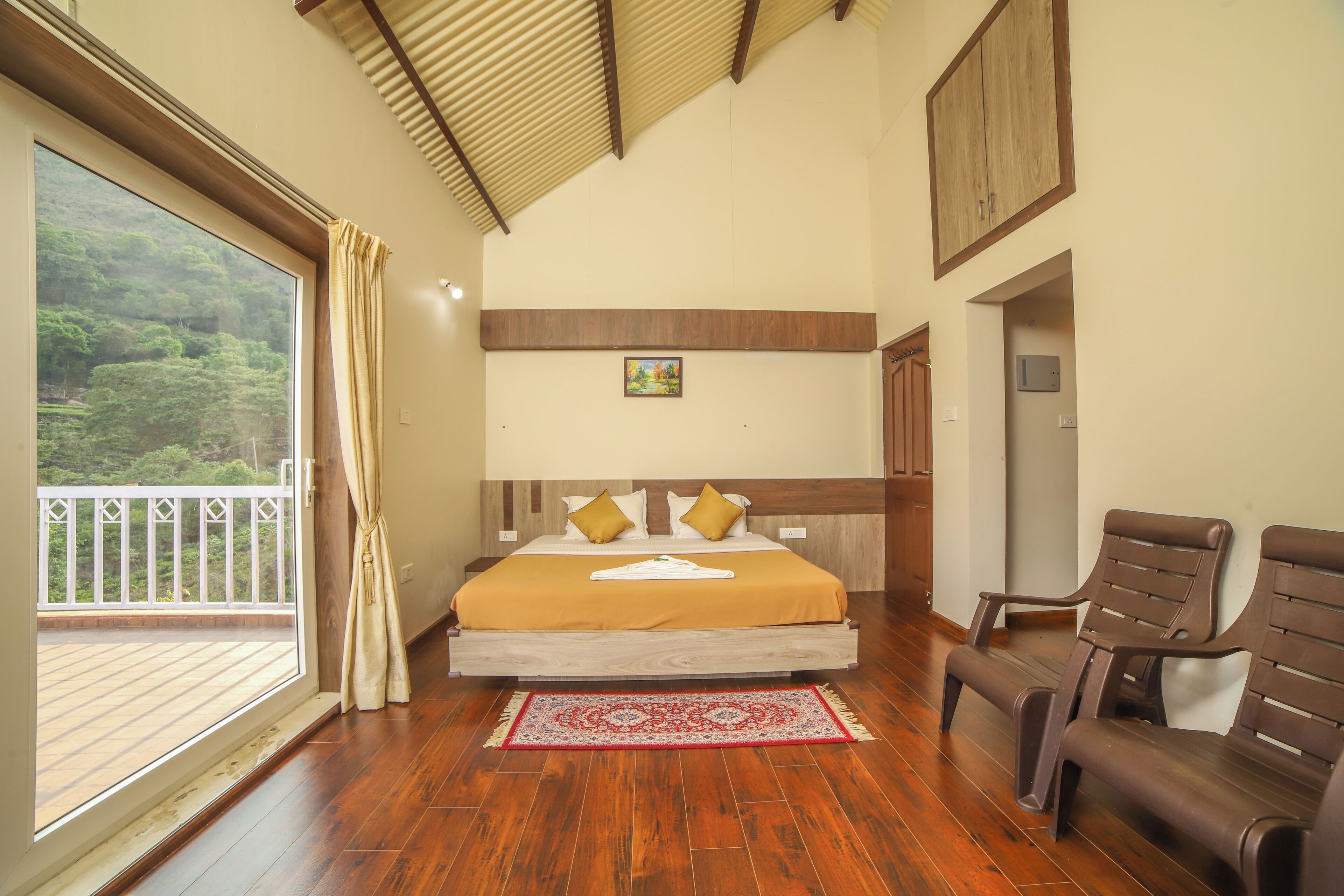 A bedroom with a large bed, wooden flooring, a balcony, and a view of greenery.