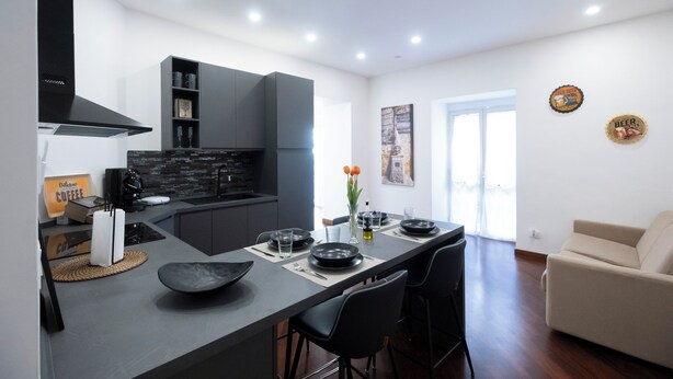 Una cocina moderna con una isla central, armarios negros y un comedor con sofá y sillas.