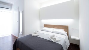 Una habitación de hotel moderna con una cama, una mesita de noche y una lámpara fijada a la pared.